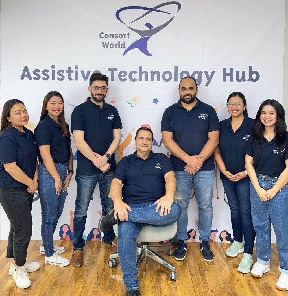 The Consort World team standing together in front of the Assistive Technology Hub banner